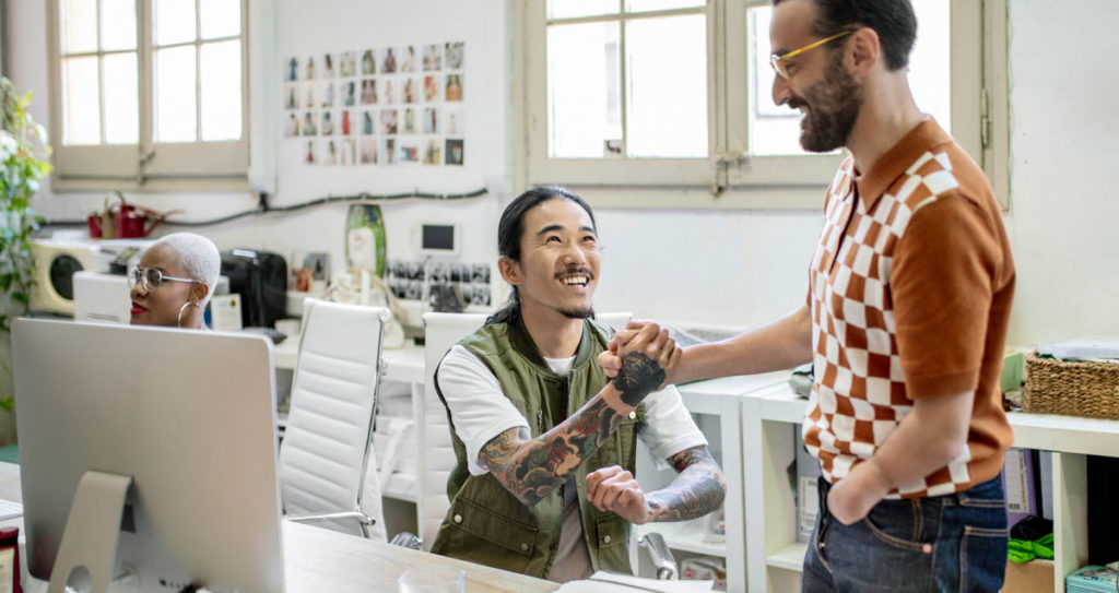 Male creative professionals shaking hands while chatting at a desk.