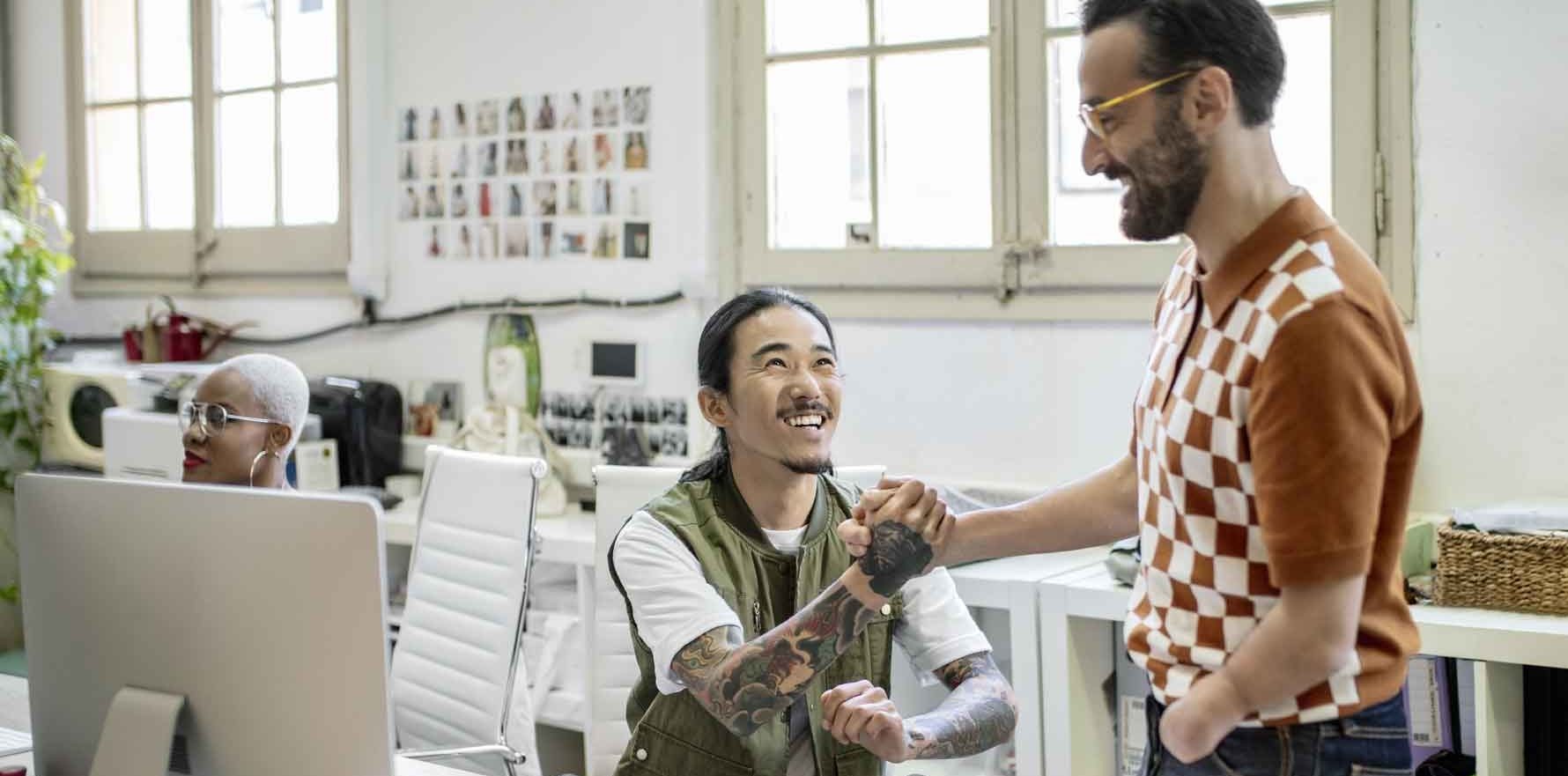 Male creative professionals shaking hands while chatting at a desk.