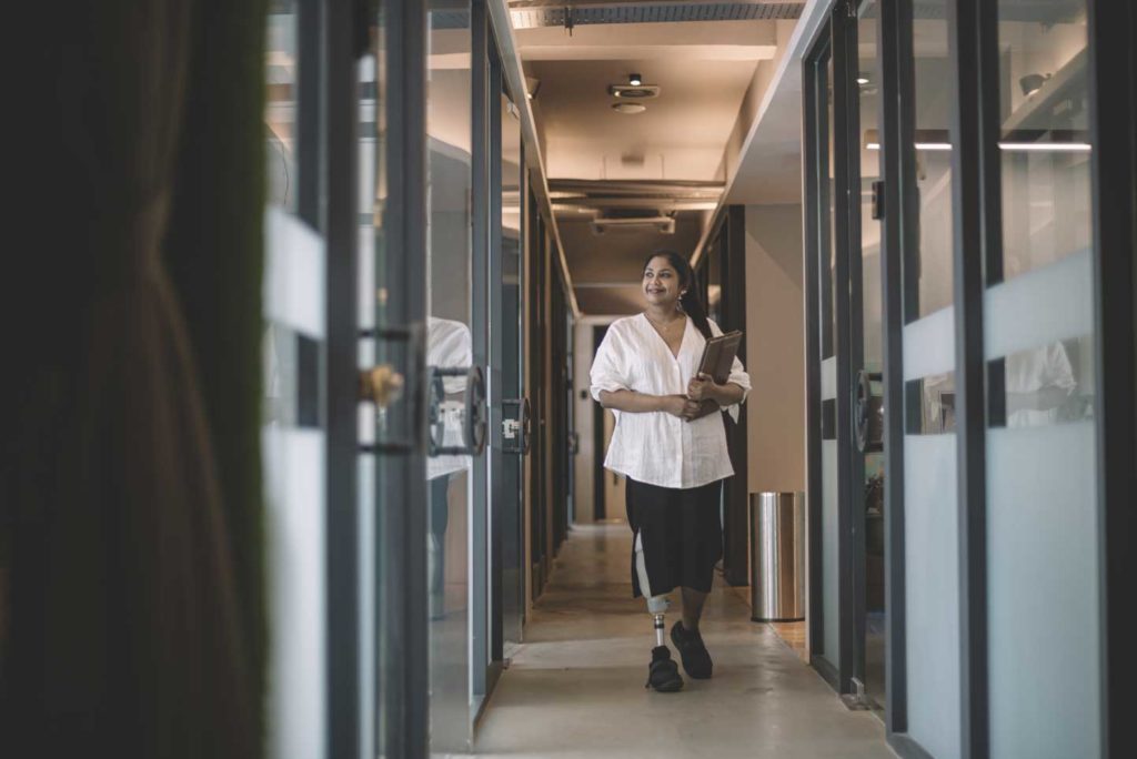 Female employee with a prosthetic leg walking along an office corridor.